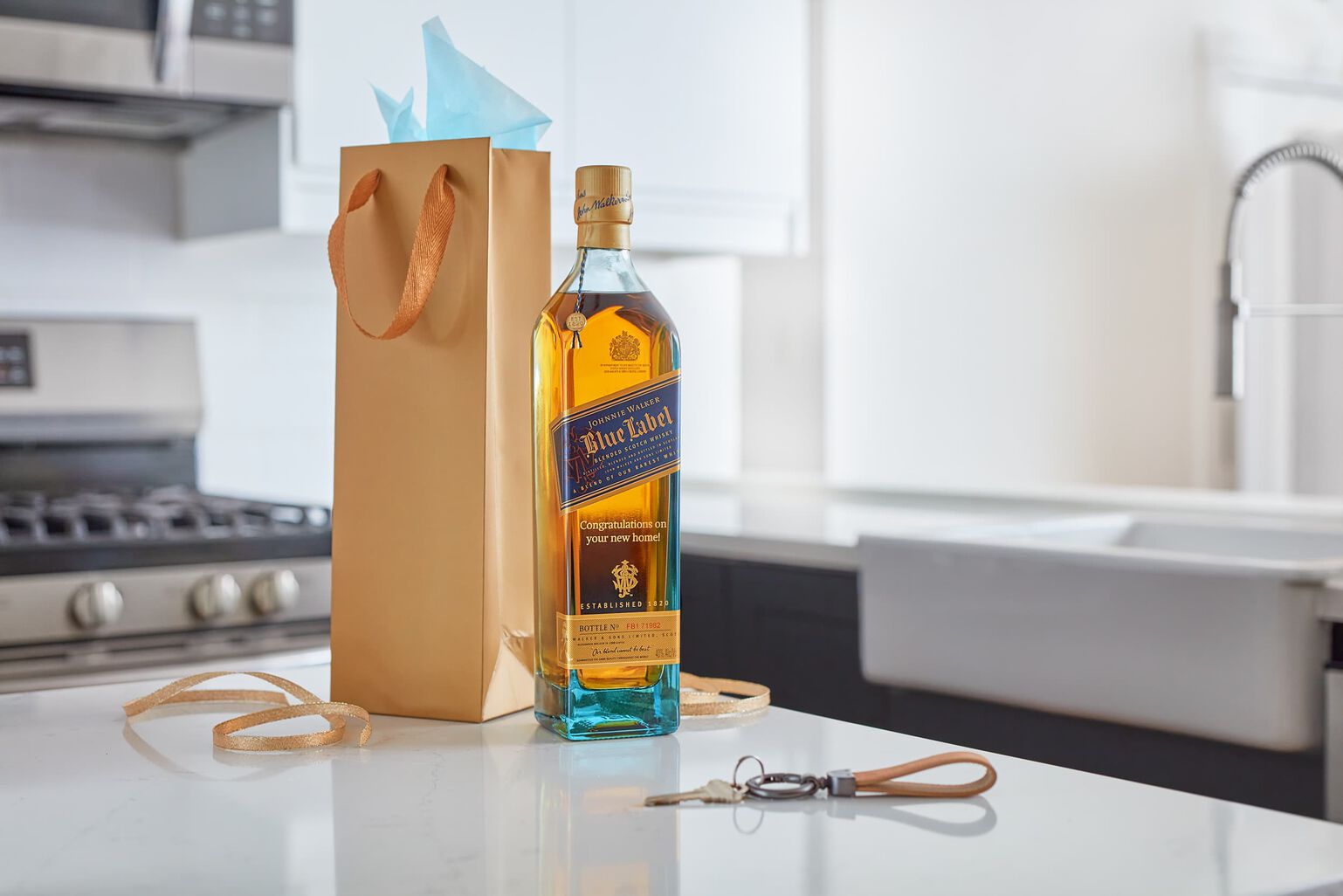 A bottle of engraved Johnnie Walker blue sits on a marble countertop with the new keys to a home